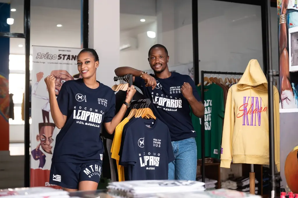 Deux supporters en t-shirts Léopards RD Congo devant un portant de la boutique